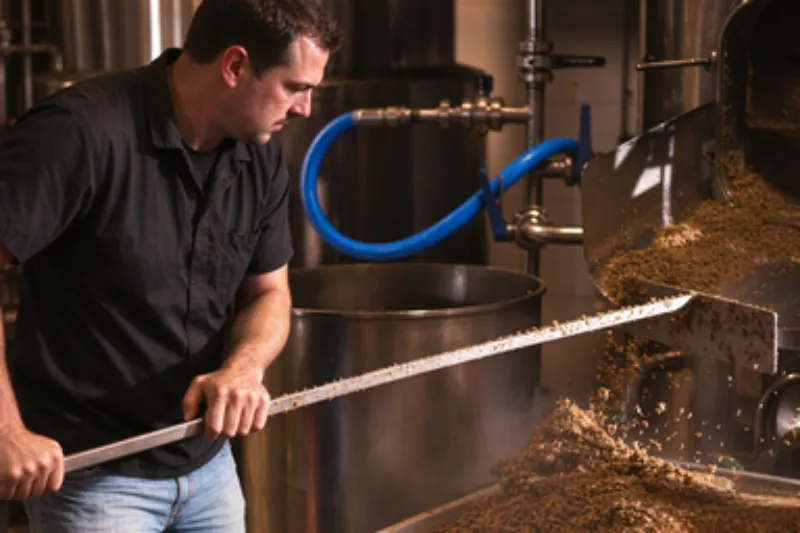 A brewer working with stainless steel beer brewing equipment during the beer brewing process in a craft brewery.